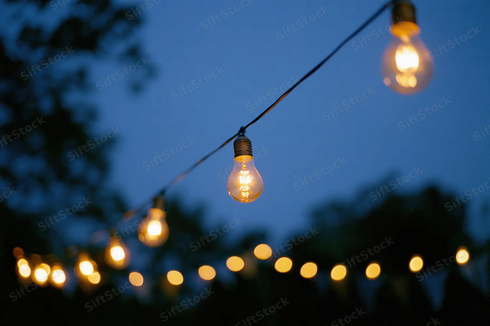 String of warm incandescent edison bulbs hanging outdoors at dusk