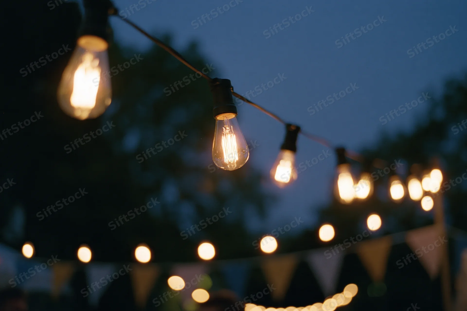 String of warm edison bulbs hanging outdoors at twilight with bunting below