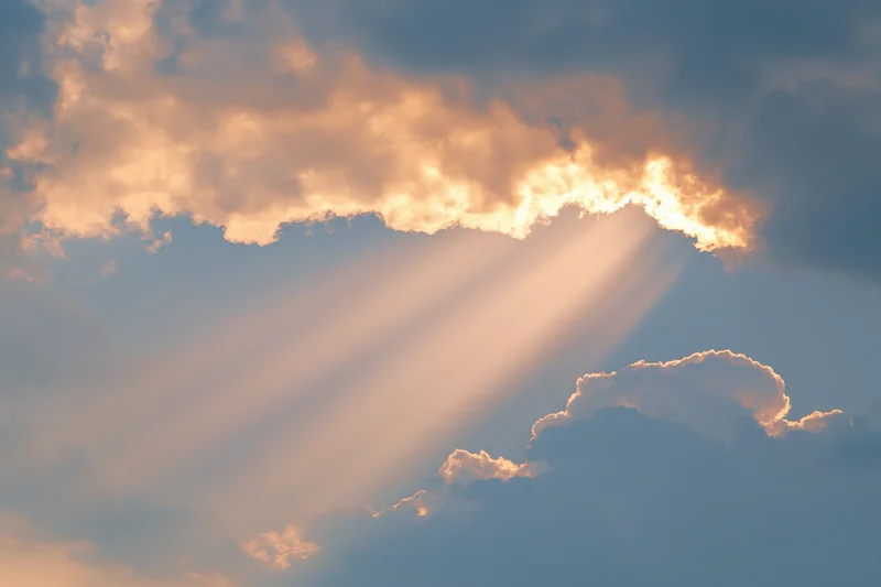 Sun rays breaking through layered cumulus clouds in a blue sky
