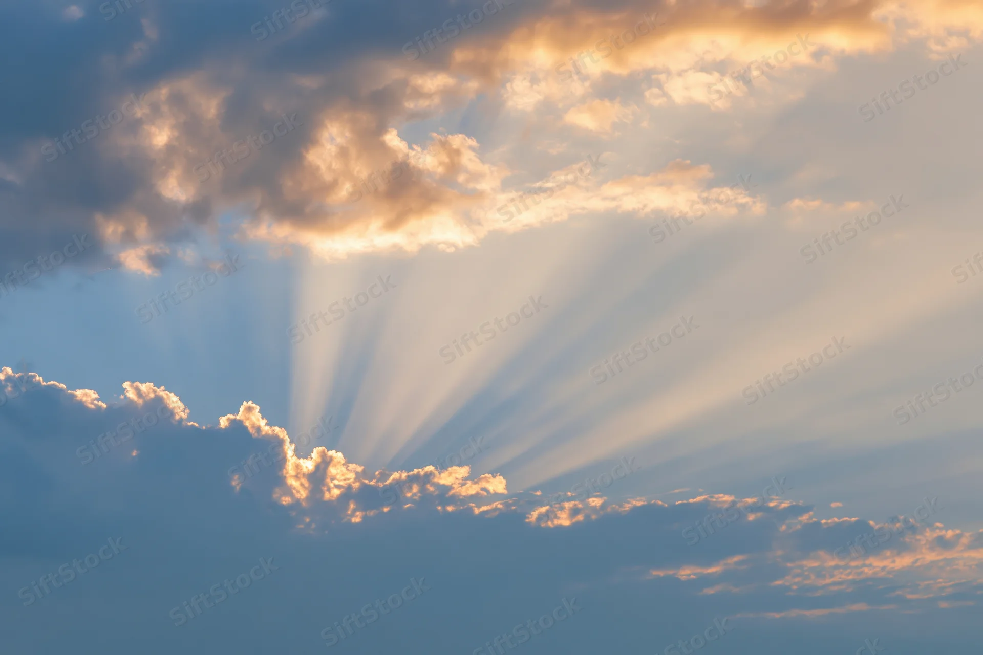 Sun rays breaking through layered cumulus clouds in a blue sky during golden hour