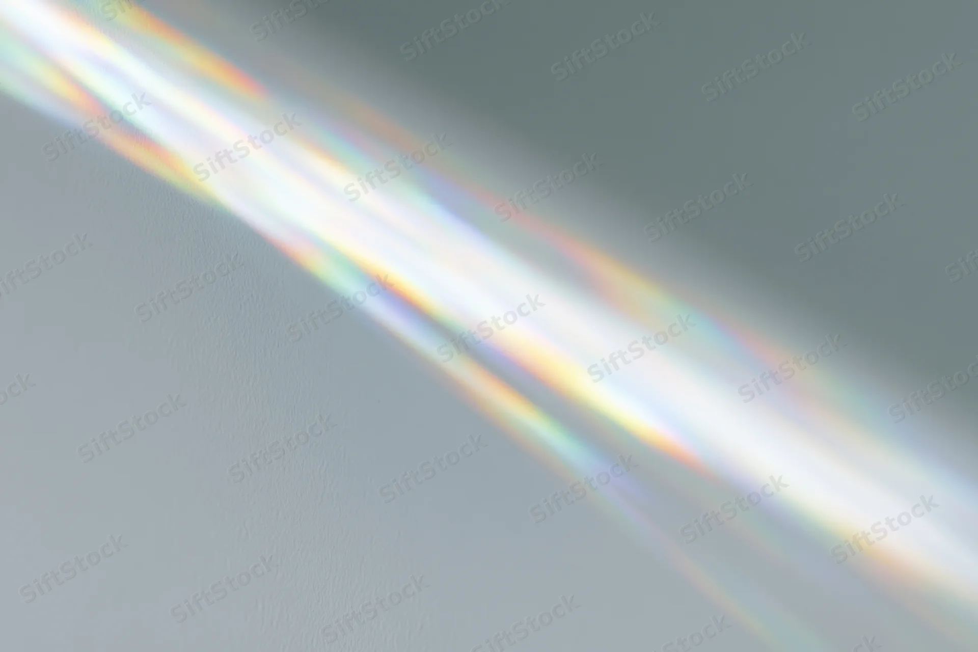 Sunlight refracting through a glass prism casting a rainbow spectrum on a gray wall
