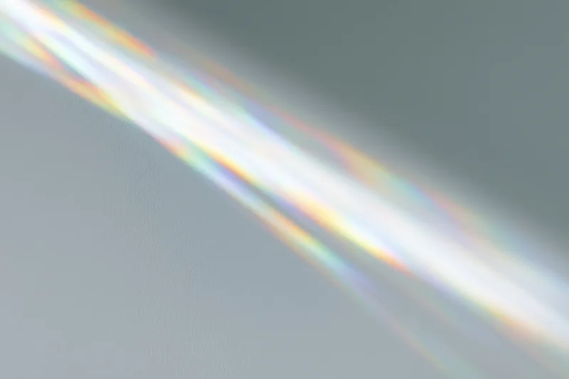 Sunlight refracting through a glass prism casting a rainbow spectrum on a gray wall