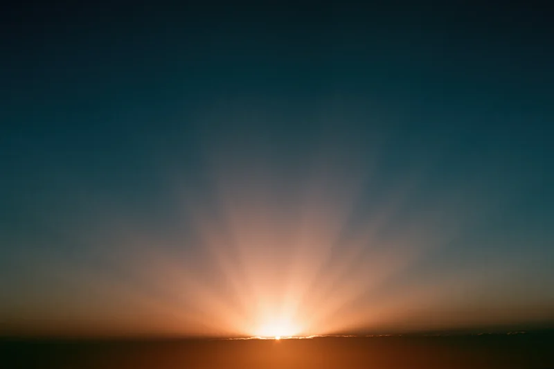 Sunrise light burst radiating upward from the horizon in a wide sky view