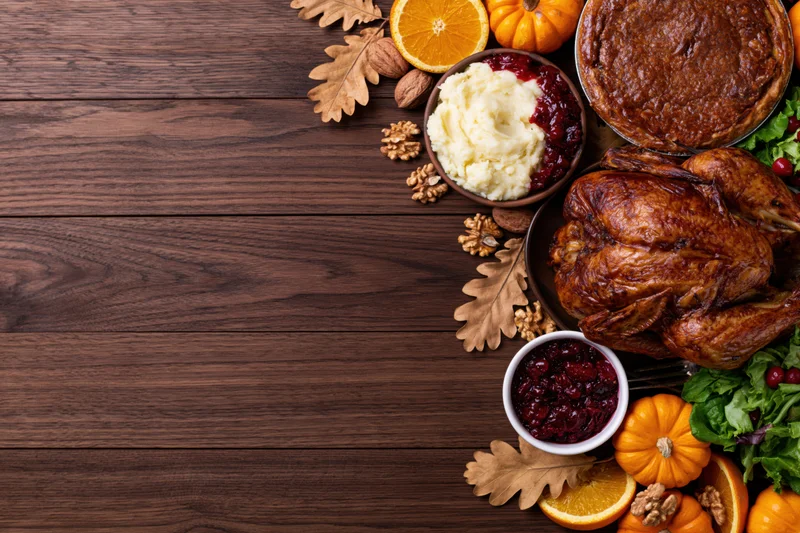 Thanksgiving dinner spread arranged along the right side of a wooden table with copyspace on the left