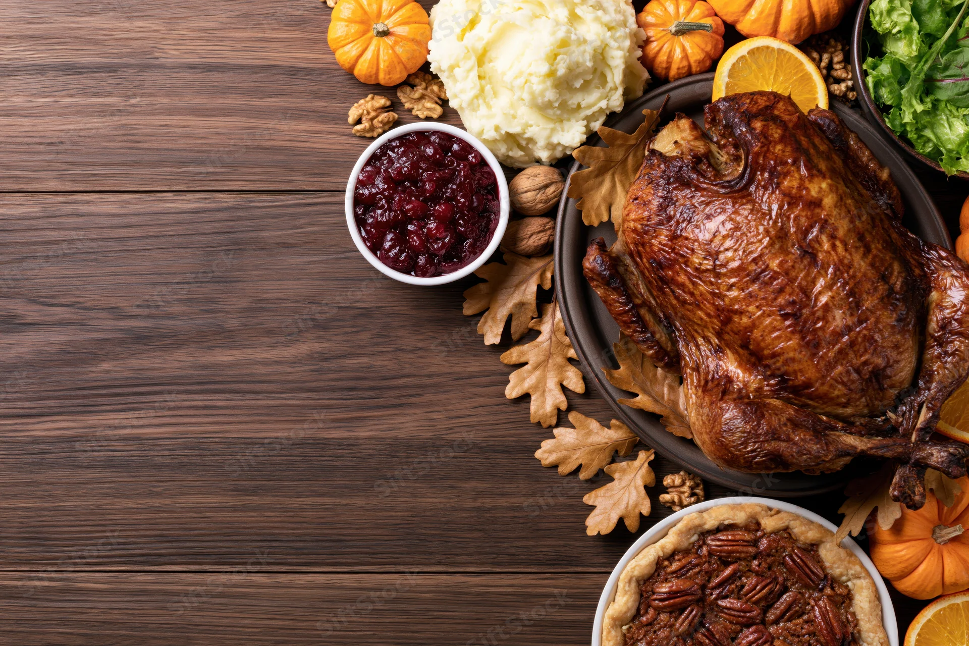 Roasted turkey and thanksgiving side dishes arranged along the right side of a wooden table with copyspace on the left
