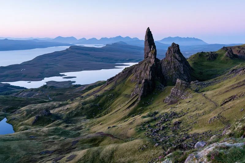 Old Man of Storr rock pinnacle rising from green highland hills overlooking lochs and distant mountains at twilight
