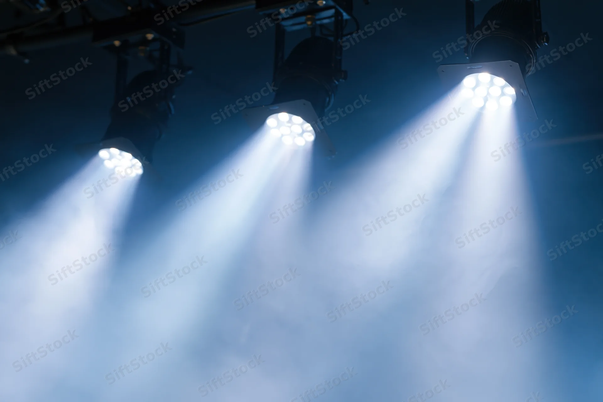 Three led par lights mounted on ceiling rig casting bright beams through smoke in dark venue