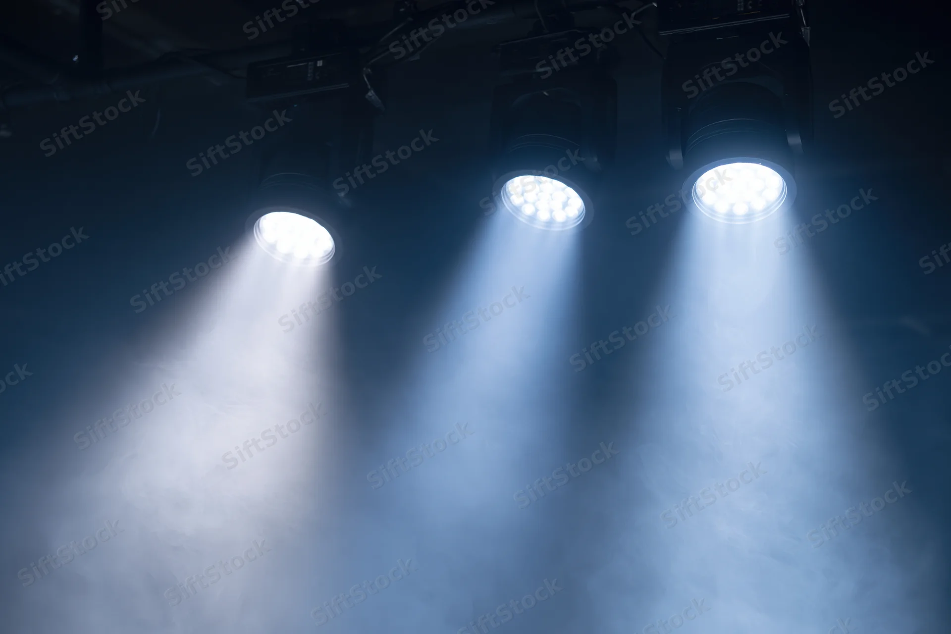 Three led par lights mounted on ceiling rig casting beams through smoke in dark venue