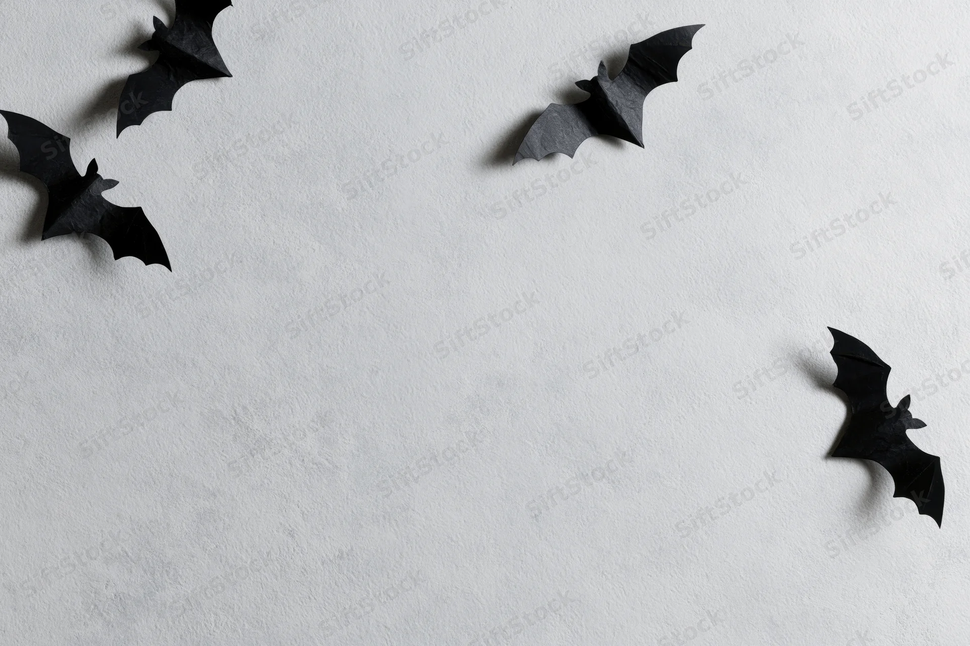 Black paper bat cutouts arranged in flying poses scattered across a white wall