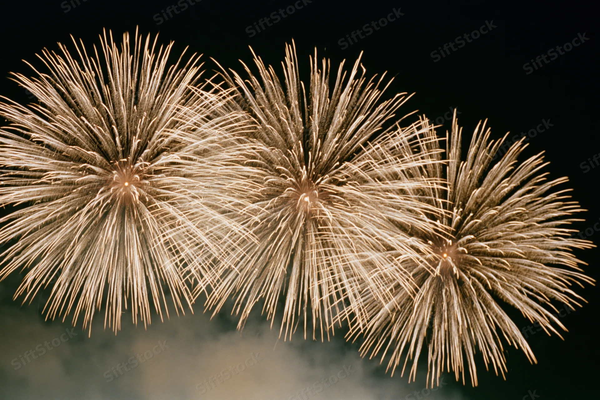 Three large fireworks bursting simultaneously across the night sky