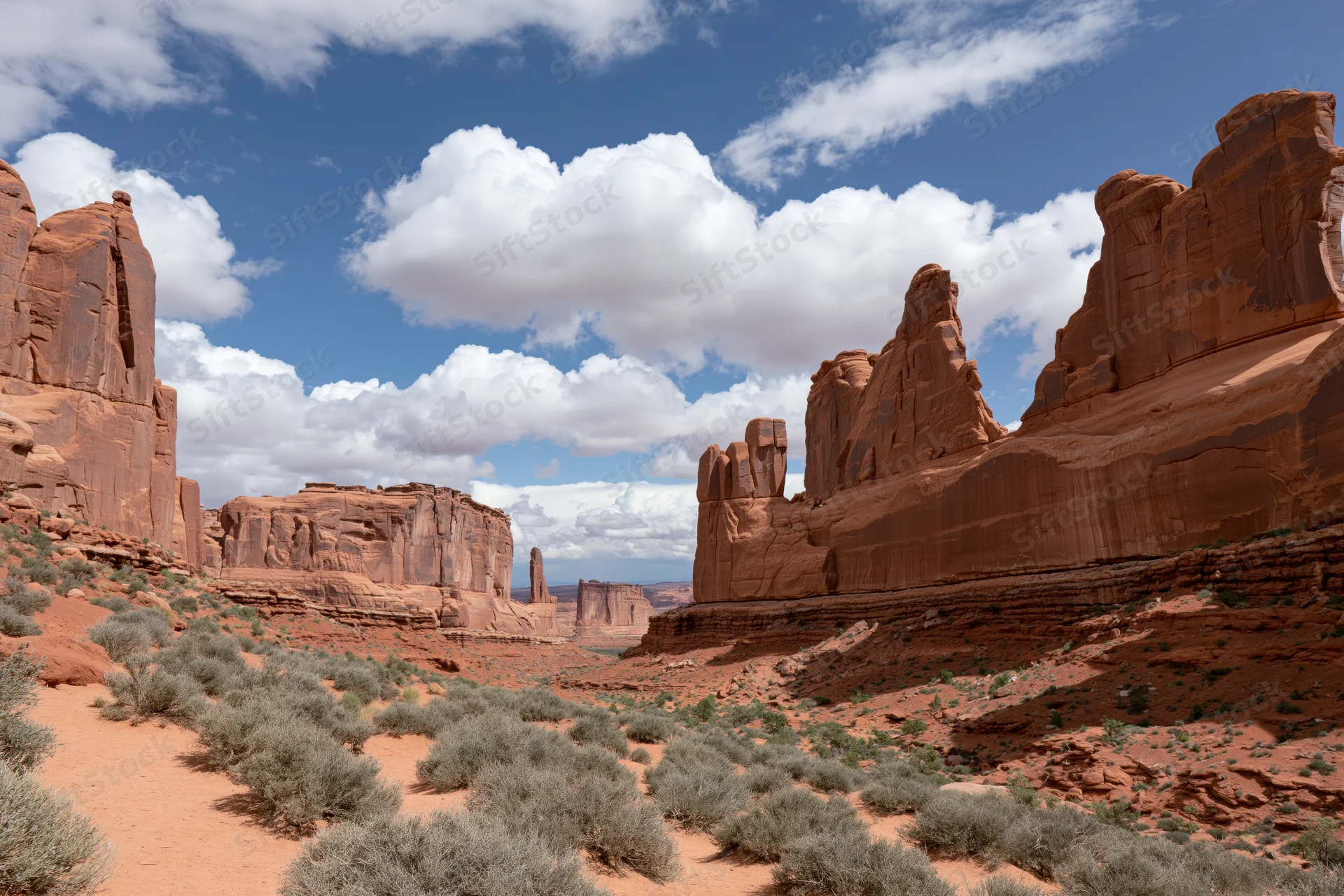Towering sandstone fins and monoliths rising from a red desert landscape under a blue sky with white clouds