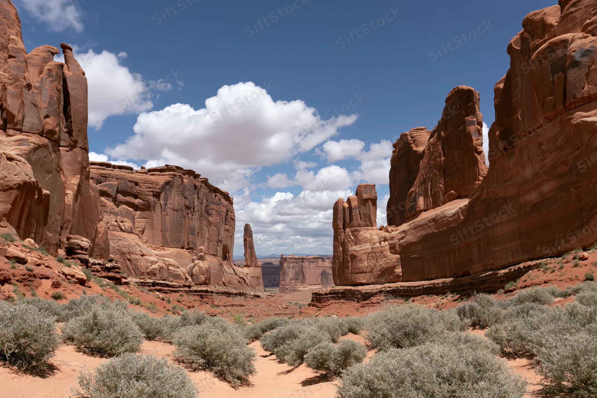 Towering sandstone fins and monoliths rising from a red desert landscape under a blue sky with white clouds