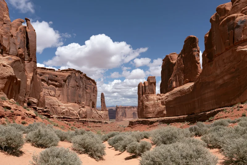 Towering sandstone fins and monoliths rising from a red desert landscape under a blue sky with white clouds