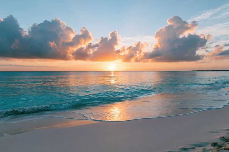Tropical beach at sunset viewed from wet sand with waves lapping shore and clouds glowing above ocean horizon
