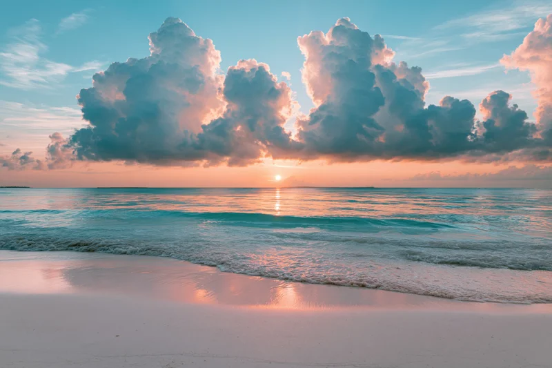 Tropical beach at sunset viewed from wet sand with waves rolling in and clouds above the horizon