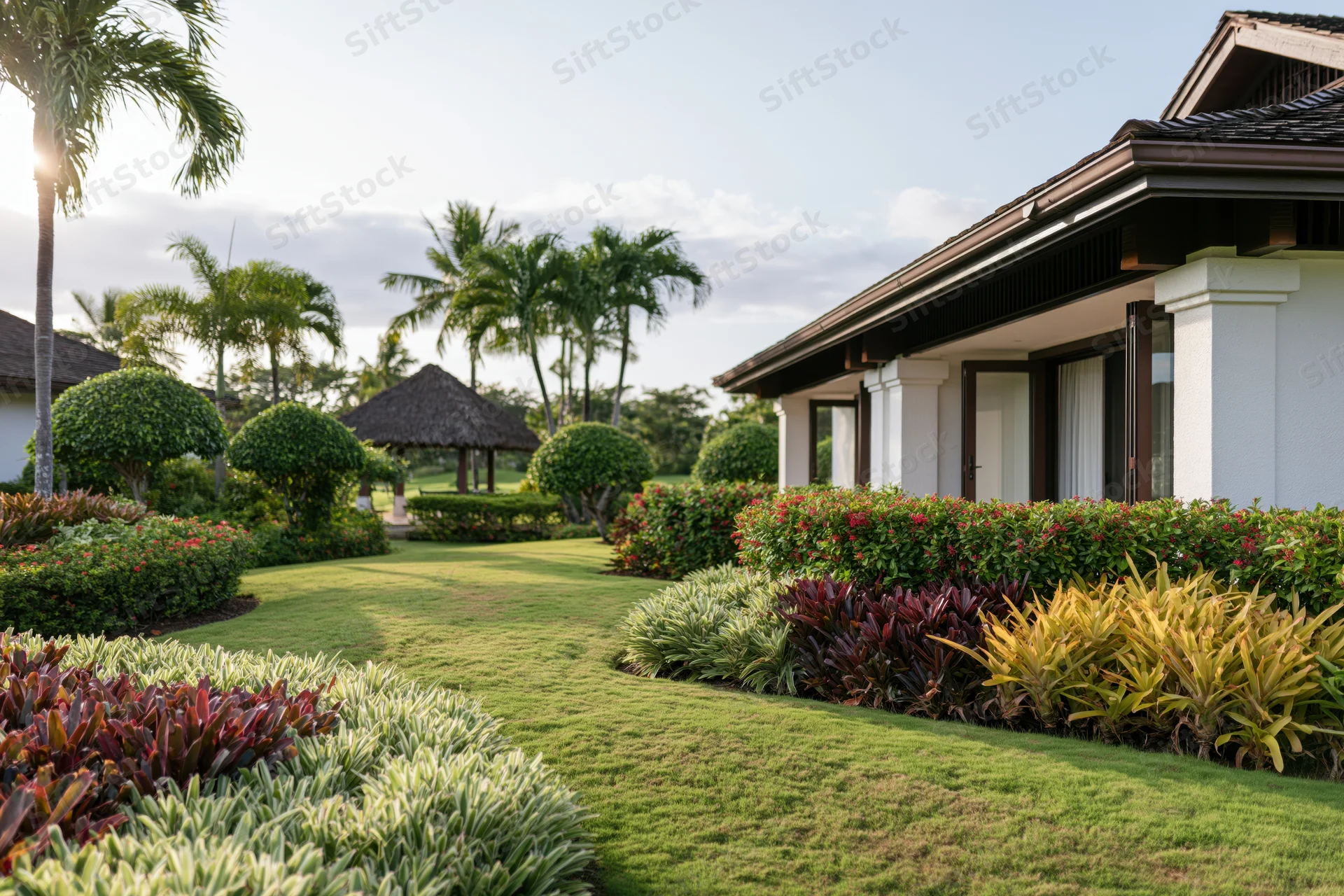 Tropical resort villa exterior with manicured garden and palm trees along a grass pathway
