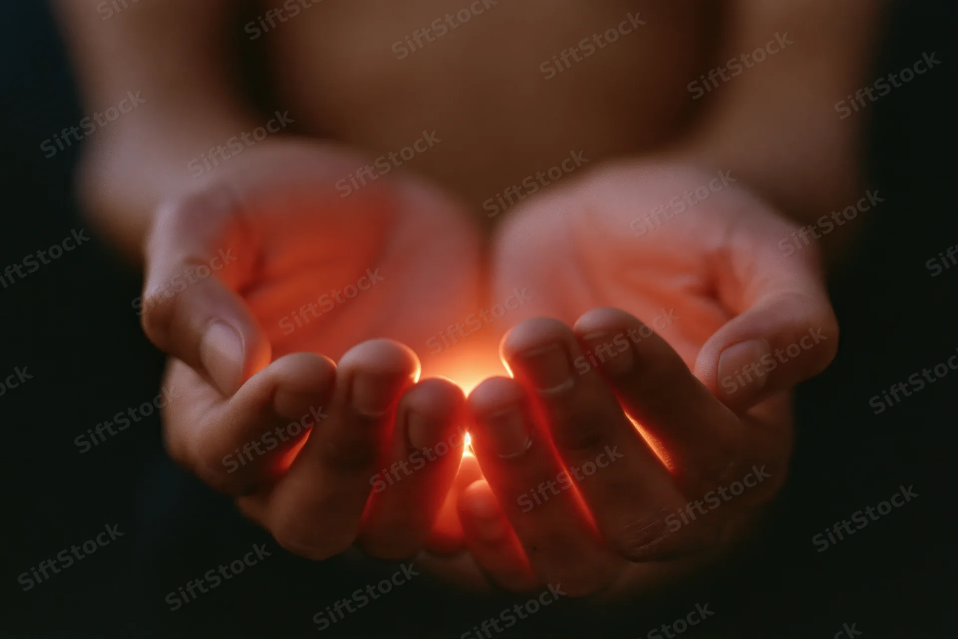 Cupped hands holding a small glowing light source in darkness