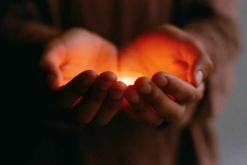 Cupped hands holding a small glowing candle in dim light