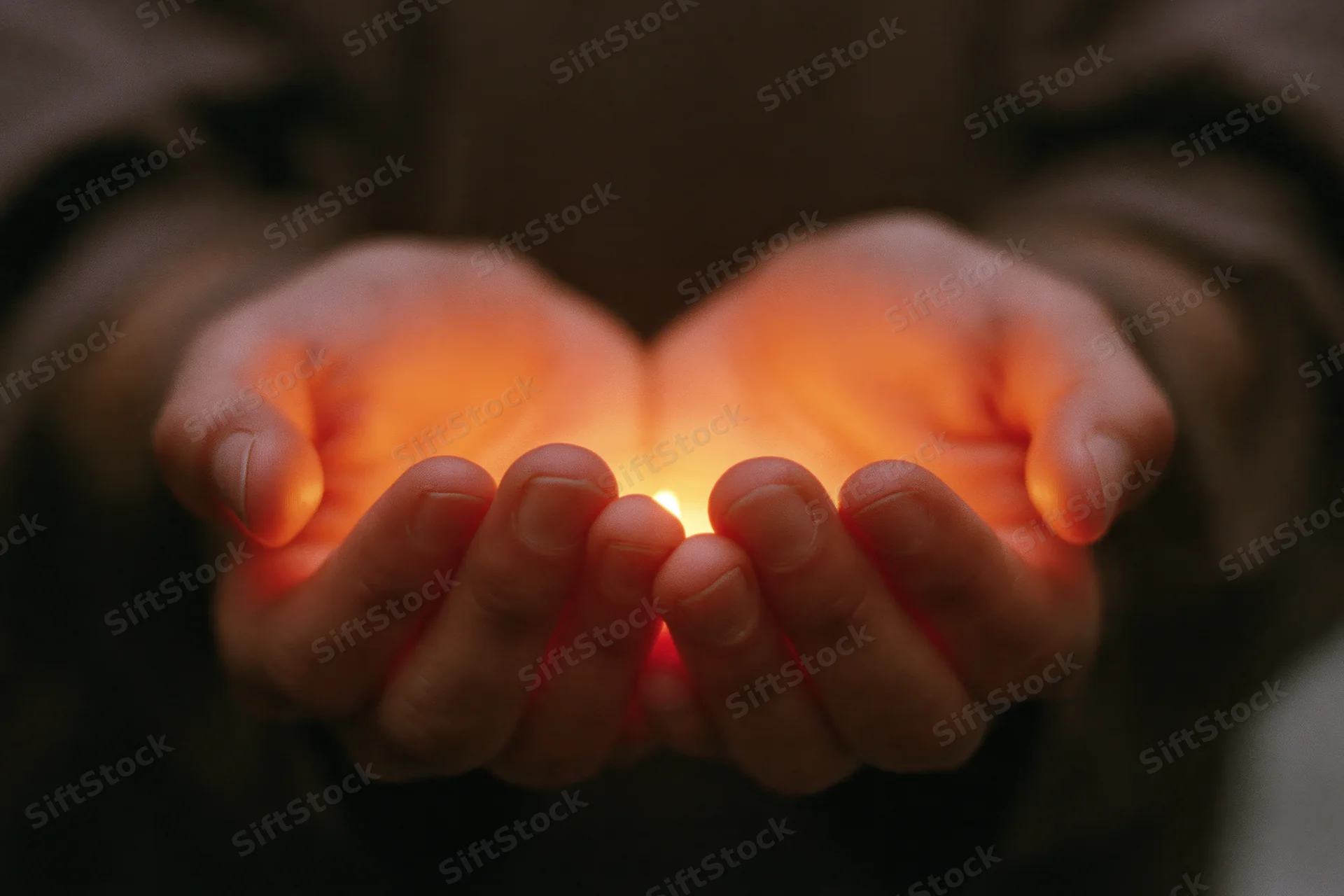 Cupped hands holding a small glowing candle in dim light
