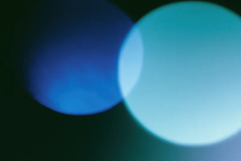 Two overlapping soft light leaks in deep electric blue and teal against dark background