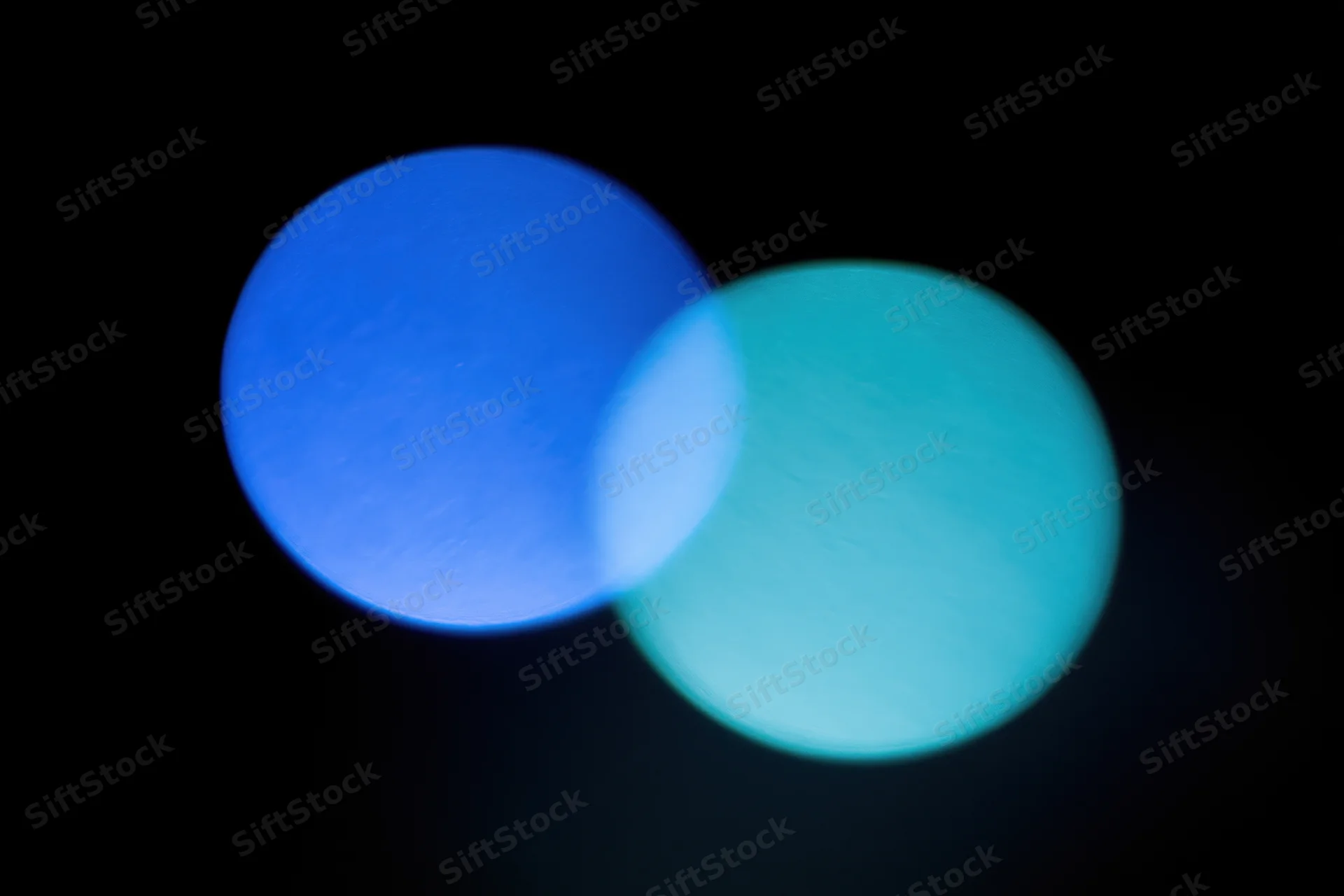 Two soft overlapping light leaks in deep electric blue and teal against black background