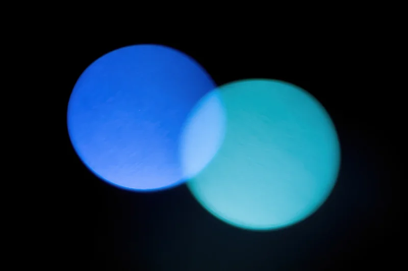 Two soft overlapping light leaks in deep electric blue and teal against black background