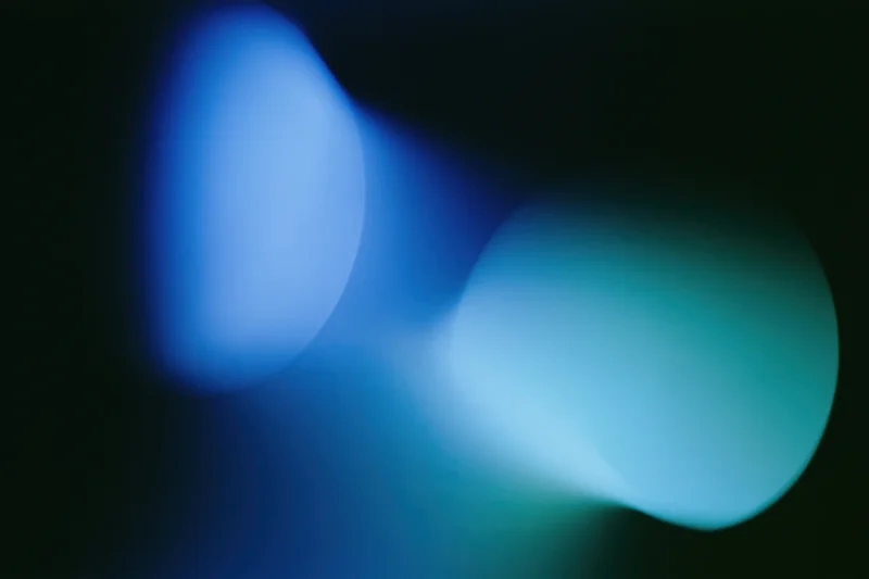 Two soft overlapping light leaks in deep electric blue and teal against dark background
