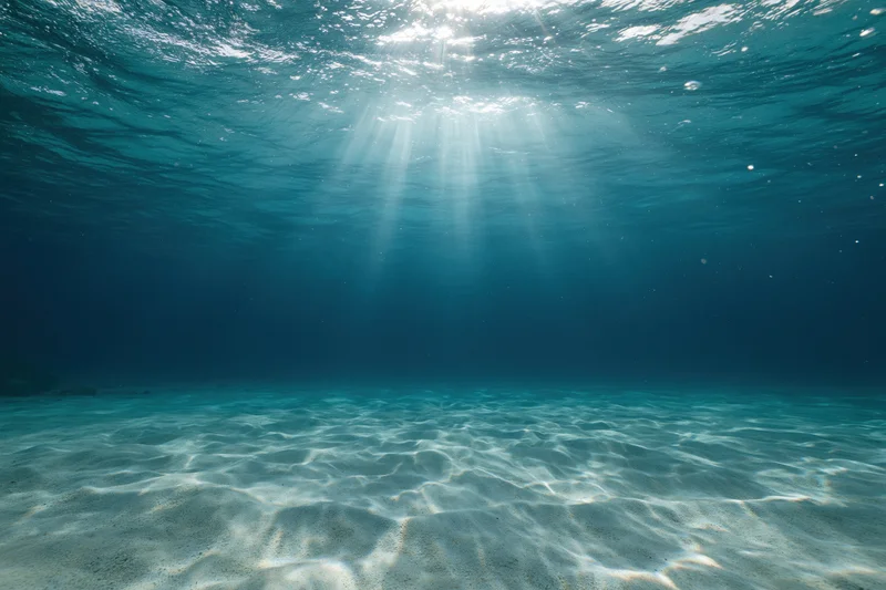 Underwater view of sandy seabed with sunlight rays filtering through ocean surface