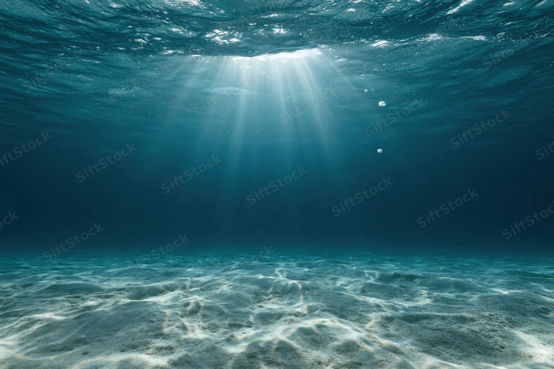 Underwater view of sandy seabed with sunlight rays filtering through ocean surface