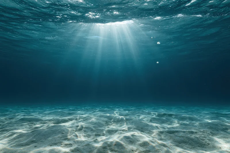 Underwater view of sandy seabed with sunlight rays filtering through ocean surface