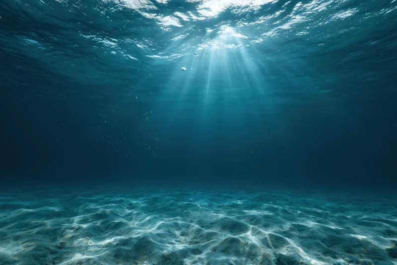 Underwater view of sandy seabed with sunlight rays filtering through ocean surface