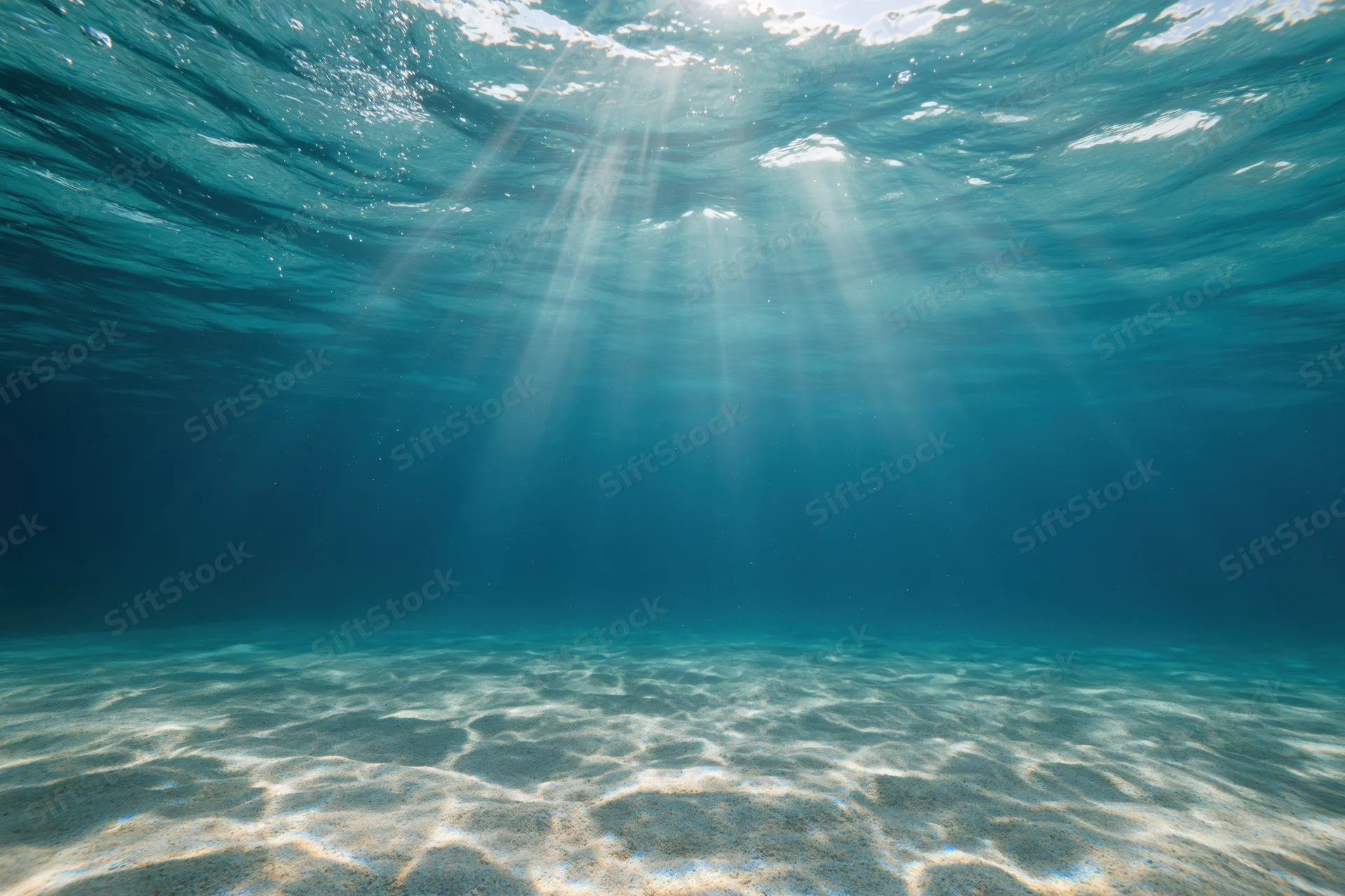 Sunlight rays penetrating ocean surface above sandy seabed
