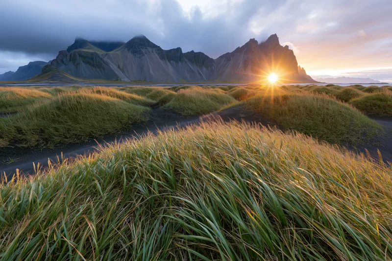 Vestrahorn mountain range rising behind rolling grass-covered dunes at sunset along the black sand coast