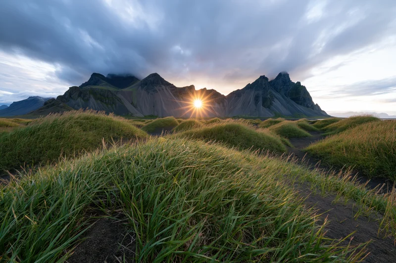 Vestrahorn mountain range rising behind rolling grass-covered fields at sunrise