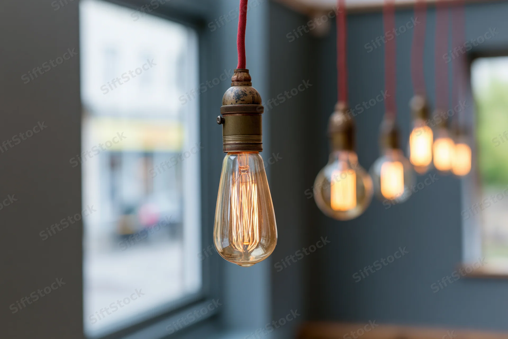 Vintage edison filament bulbs hanging from red cloth cables in interior space with blurred window background