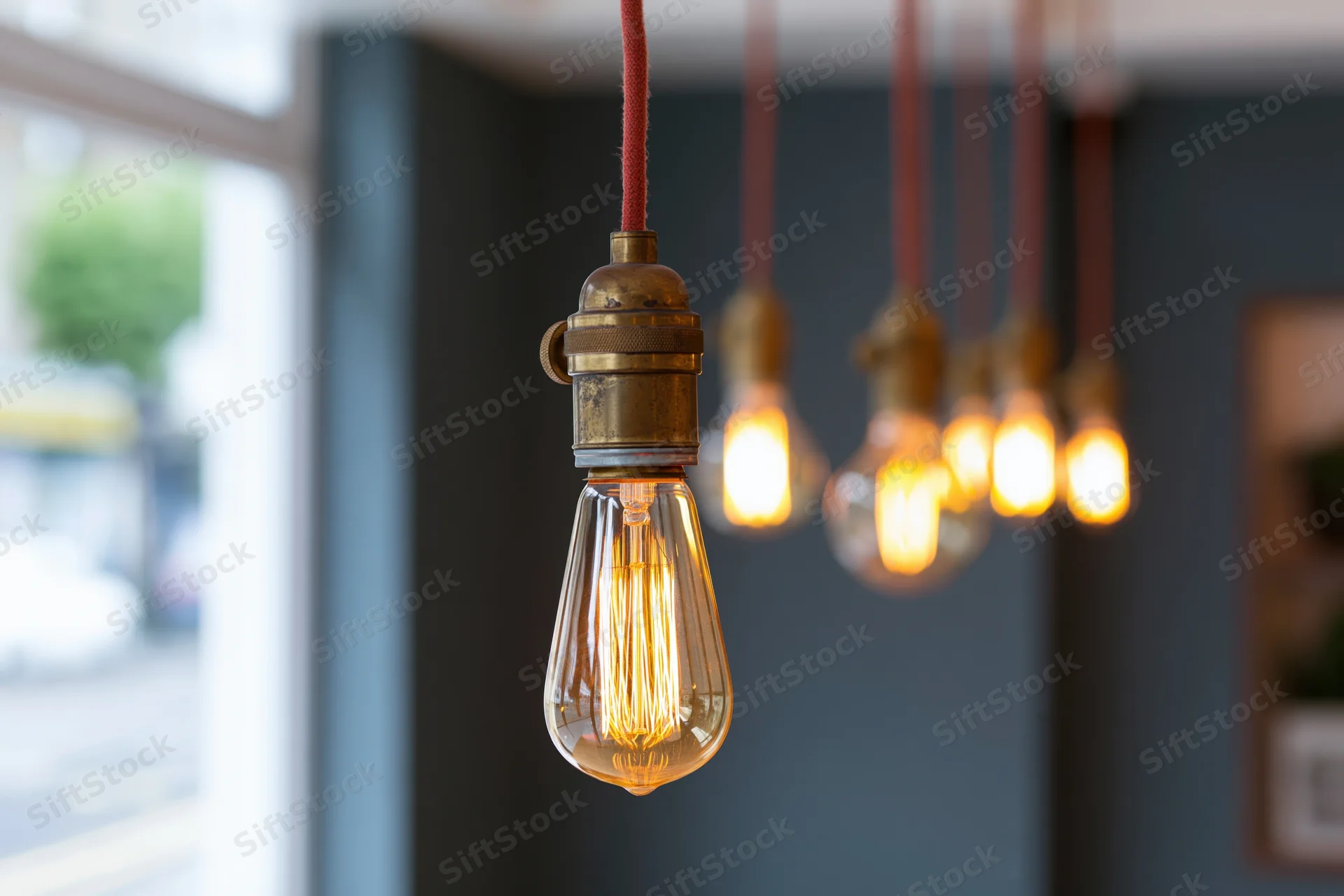 Vintage edison filament bulbs hanging from red cloth cables in interior space with soft focus background