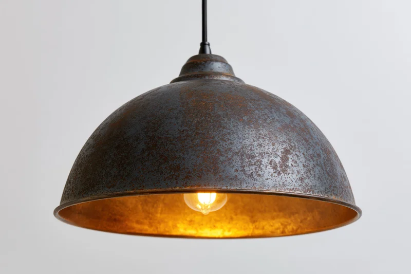 Vintage industrial dome pendant lamp hanging from ceiling with warm glowing bulb inside rusted metal shade