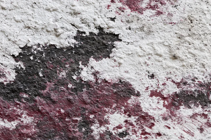 Weathered concrete wall with peeling white and red paint revealing gray surface