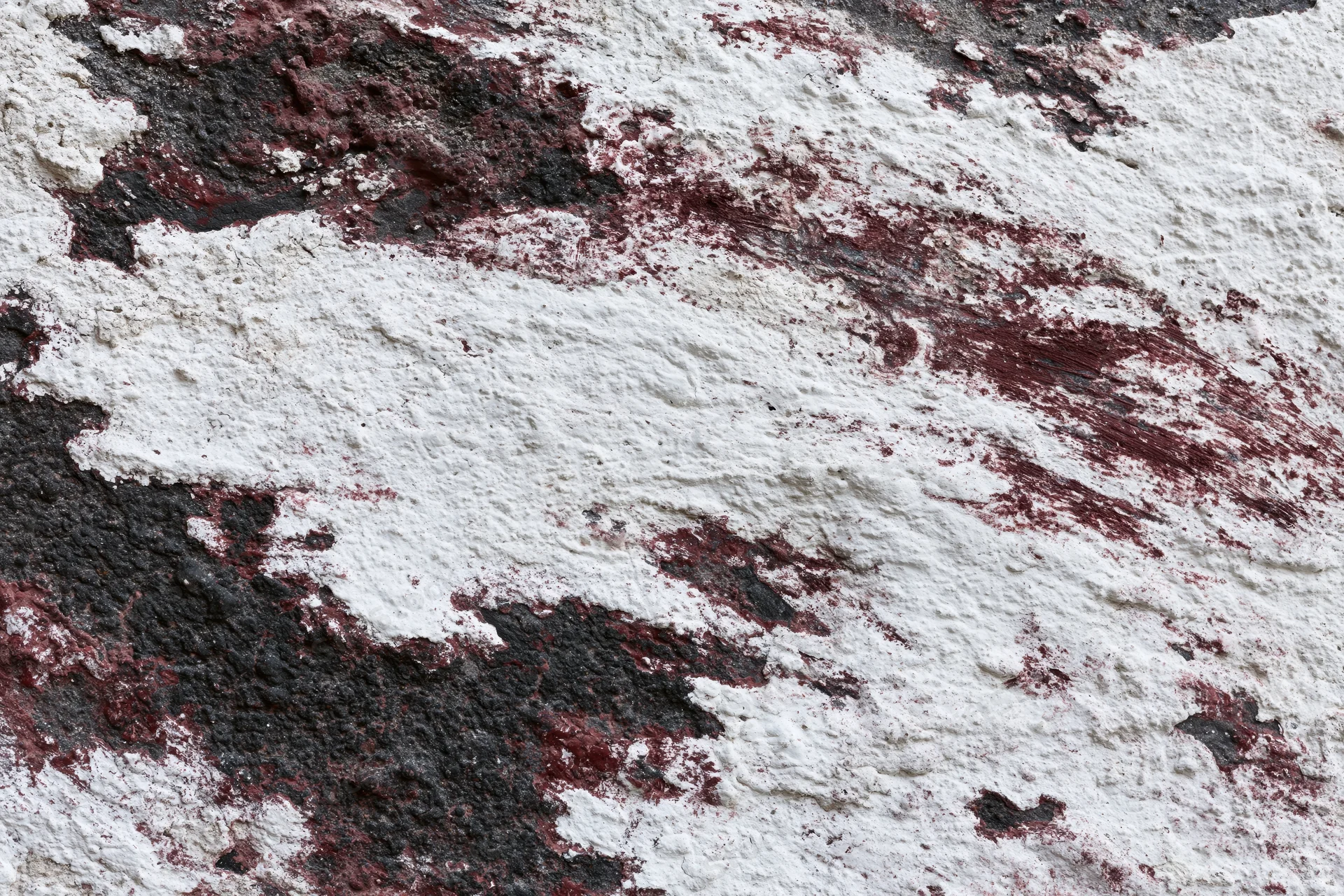 Weathered concrete wall with peeling white and red paint showing black underlayer