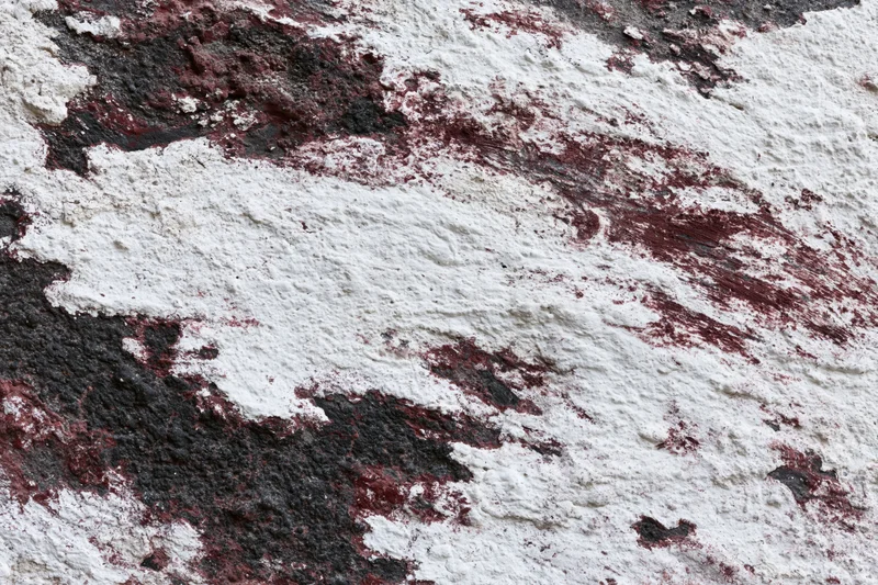 Weathered concrete wall with peeling white and red paint showing black underlayer