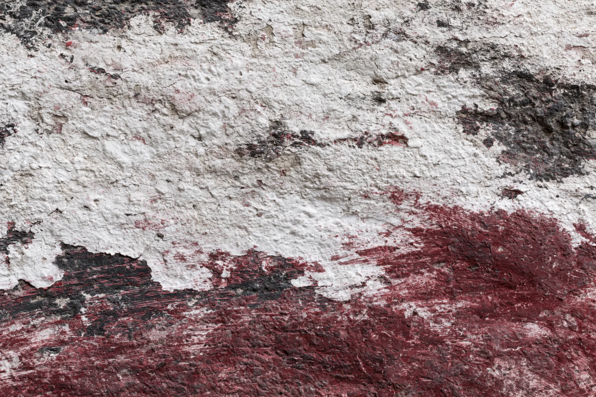 Weathered concrete wall with peeling red and white paint showing underlying surface