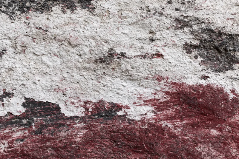 Weathered concrete wall with peeling red and white paint showing underlying surface