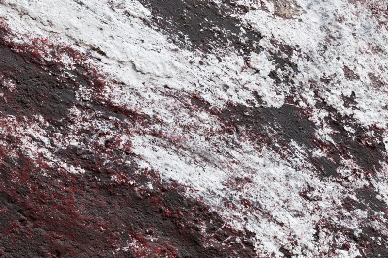 Weathered concrete wall with peeling red and white paint showing underlying dark surface