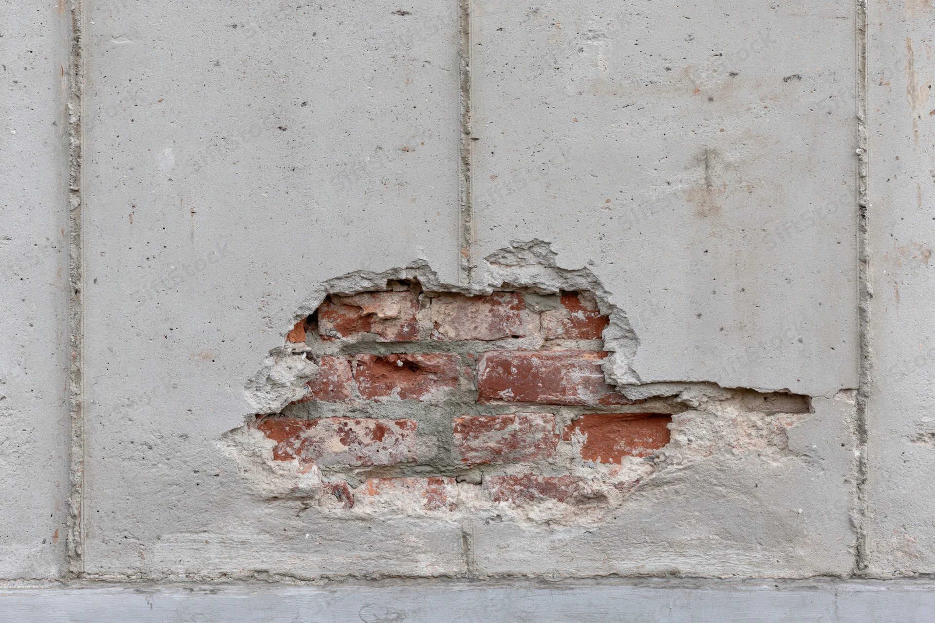 Damaged concrete wall with exposed red bricks and cracked plaster on exterior building facade