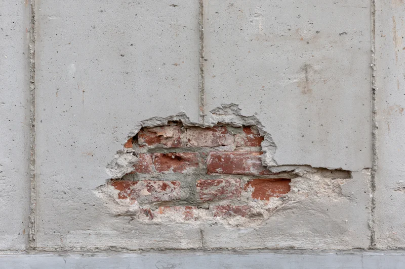 Damaged concrete wall with exposed red bricks and cracked plaster on exterior building facade