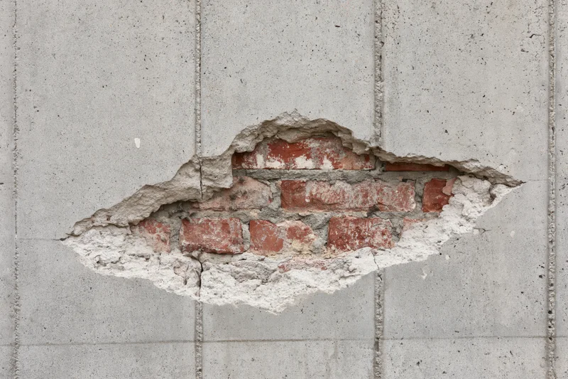 Damaged concrete wall with exposed red bricks and mortar cracks