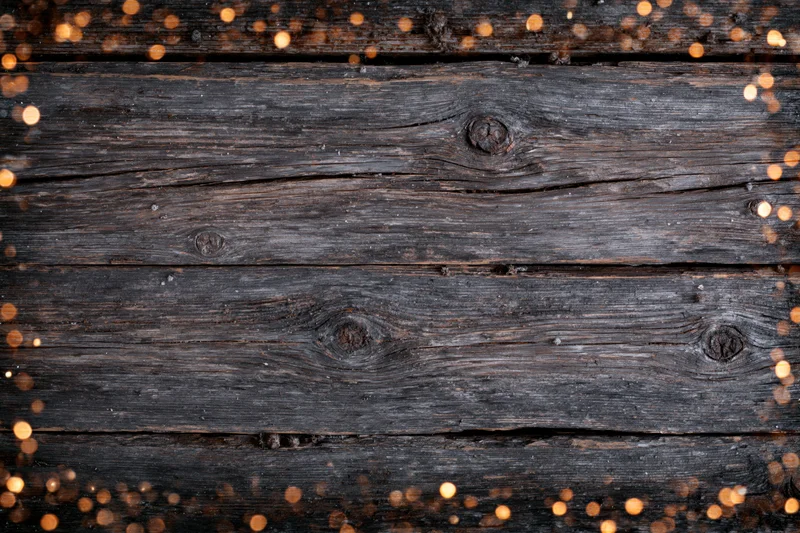 Dark weathered wooden planks arranged horizontally with warm bokeh lights around edges