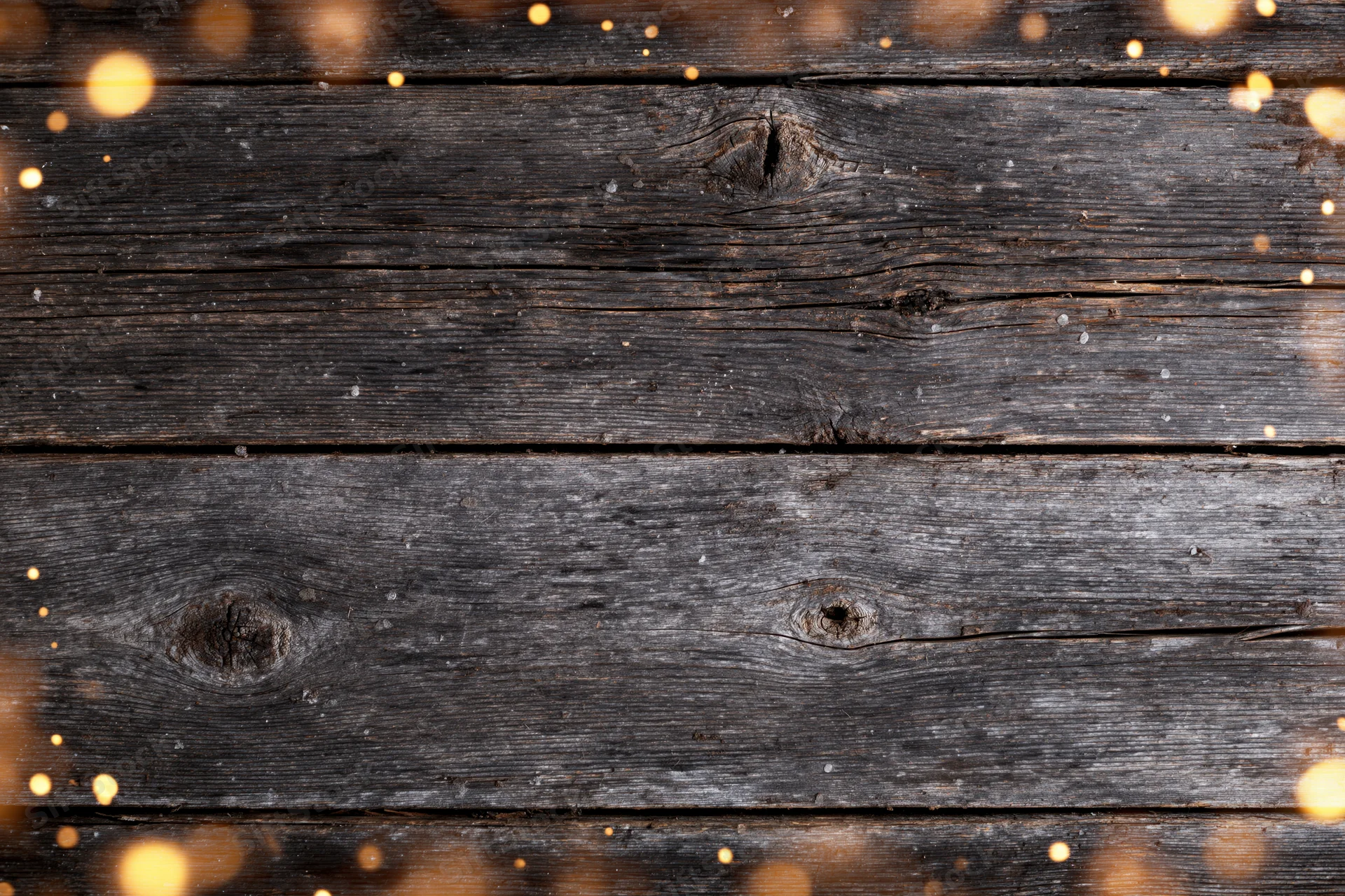 Dark weathered wooden planks arranged horizontally with golden bokeh lights around edges as background