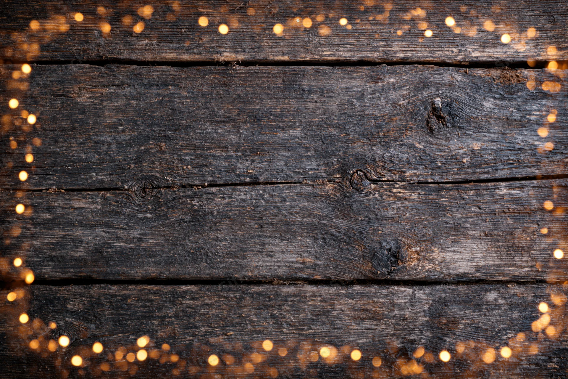 Dark weathered wooden planks arranged horizontally with warm bokeh lights framing the edges