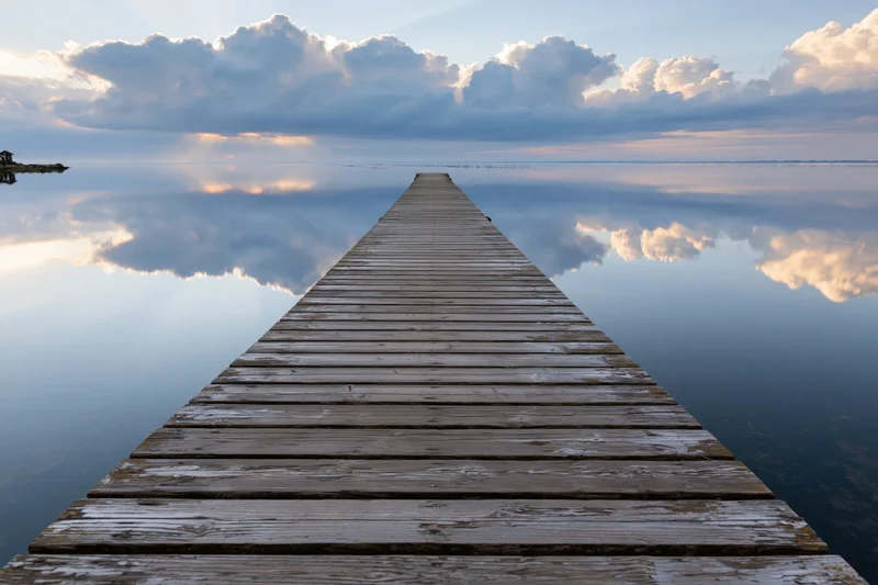 Weathered wooden dock extending into calm bay with cloud reflections at dusk